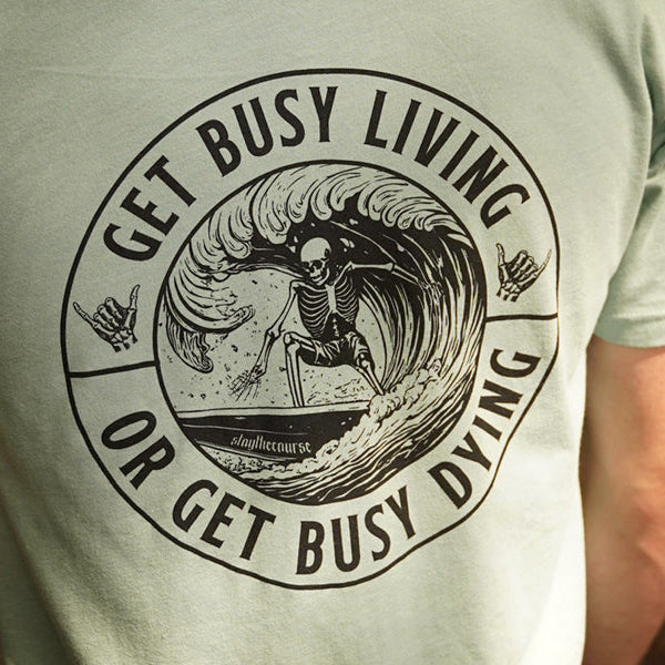 Person wearing a seafoam green t-shirt with black graphic print that says "get busy living or get busy dying"