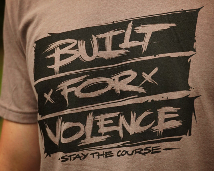 T-shirt with 'Built for Violence, Stay the Course' text on a blurred background