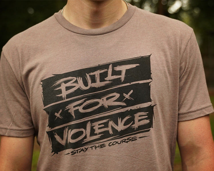 Person wearing a brown t-shirt with 'Built for Violence' graphic design.