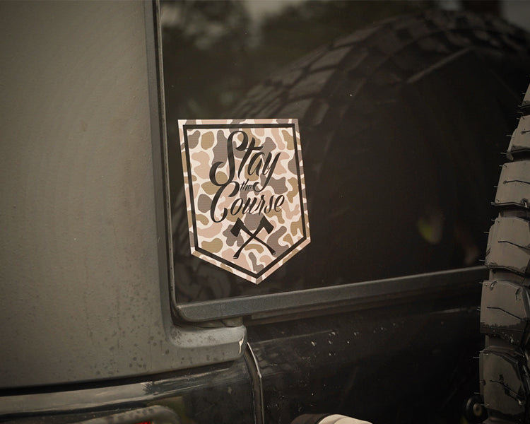 Duck Camouflage-style decal on a vehicle with 'Stay the Course' text, next to a tire.