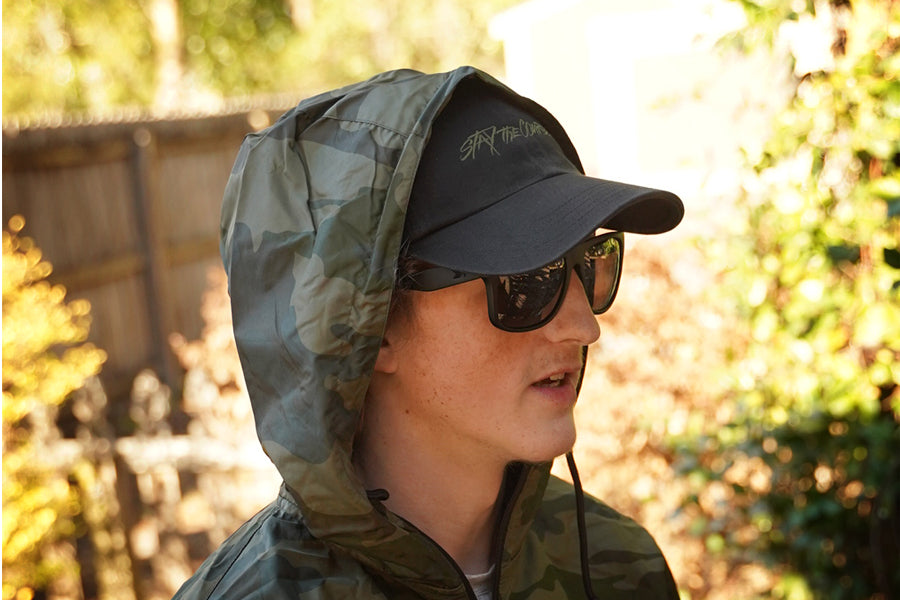 Person wearing a hooded jacket and sunglasses outdoors with blurred background