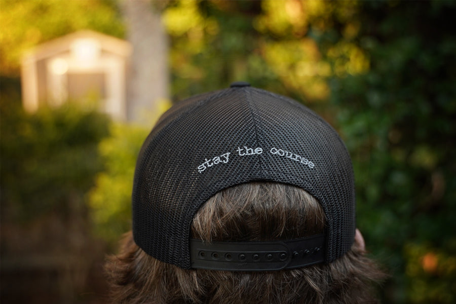Person wearing a black cap with 'stay the course' text in an outdoor setting