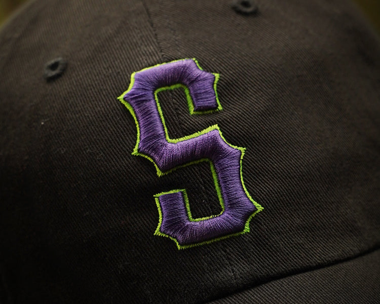 Black cap with purple and green embroidered logo on a blurred background