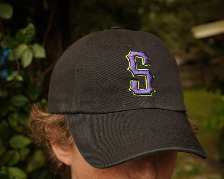 Person wearing a black cap with a purple and green logo outdoors