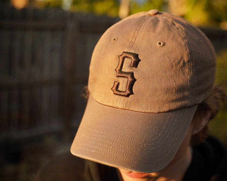 Brown baseball cap with a logo worn by a person, blurred background