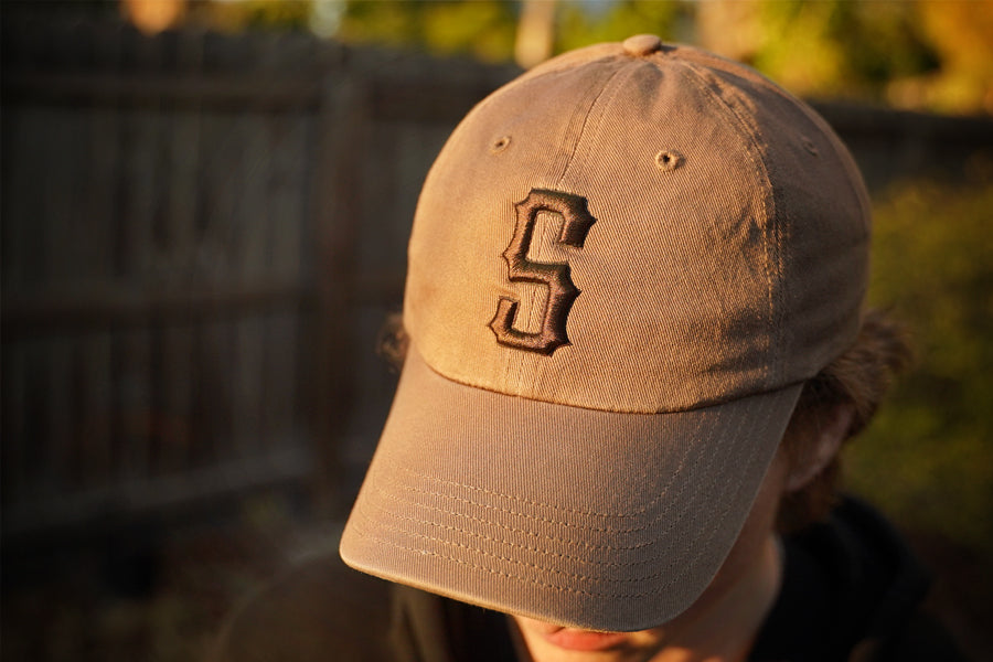 Brown baseball cap with a logo worn by a person, blurred background