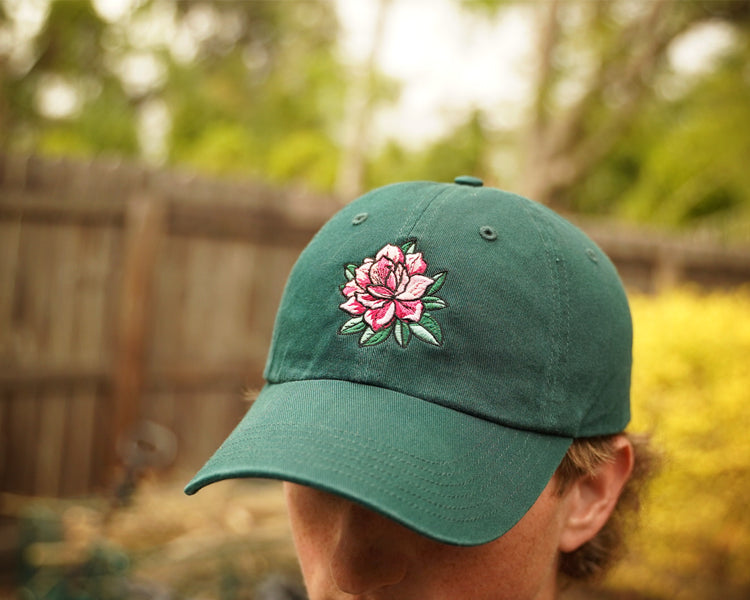 Green cap with a pink floral design worn by a person outdoors.