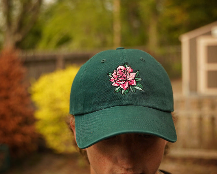 Green cap with a pink flower design worn by a person outdoors.