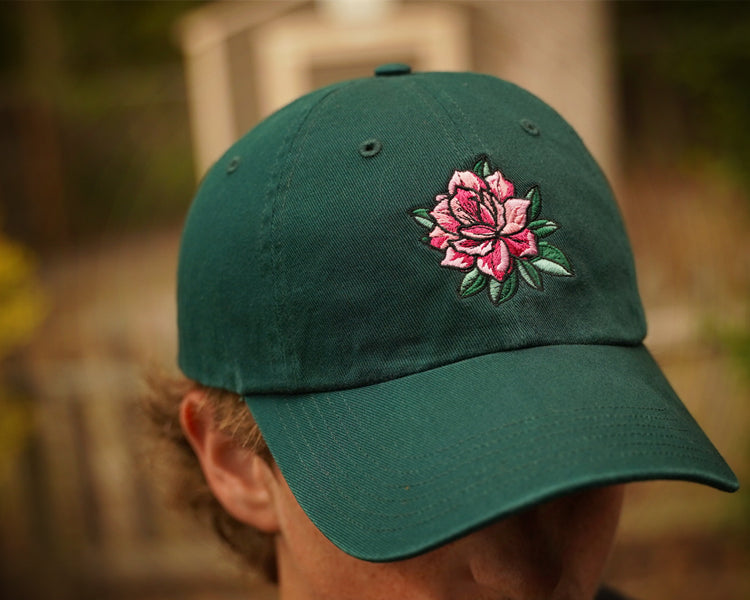 Green cap with a pink flower design worn by a person outdoors.