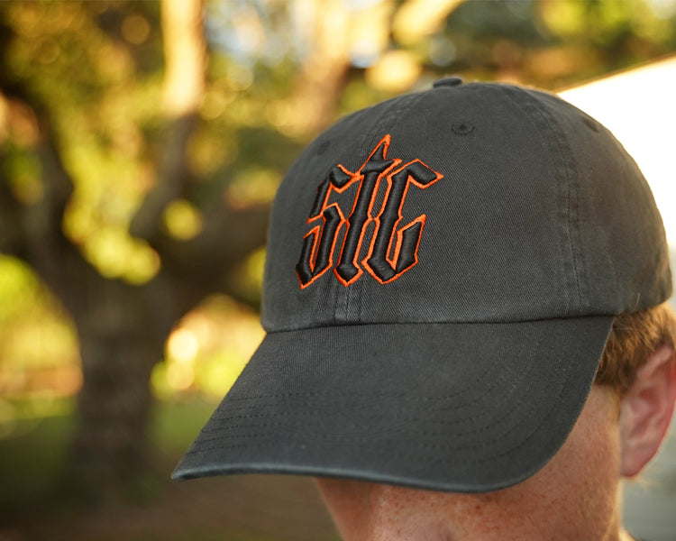 Person wearing a black hat with orange and black "stc" puff embroidery on the front, in an outdoor setting