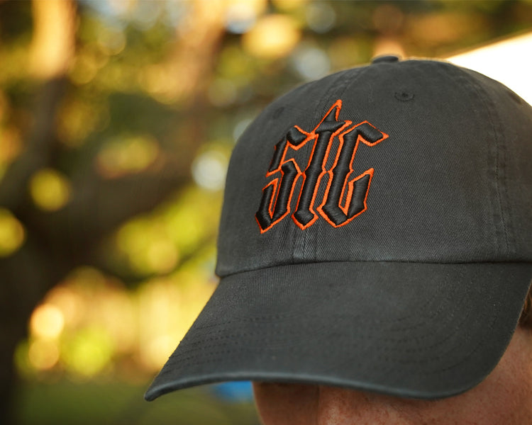 Person wearing a black hat with orange and black "stc" puff embroidery on the front, in an outdoor setting