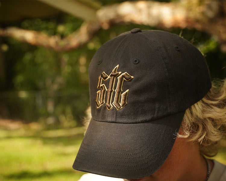 Black cap with gold and brown logo worn by a person outdoors