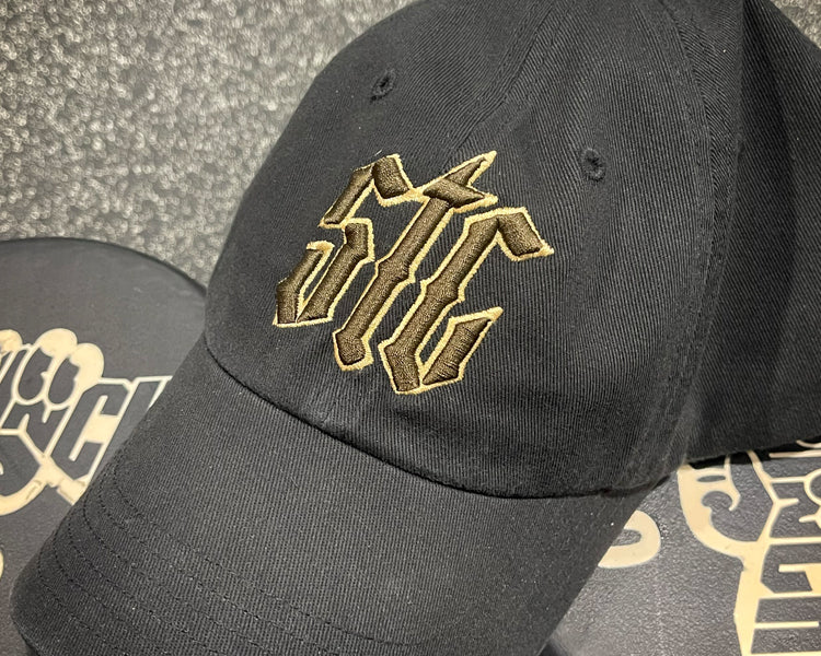 Black cap with gold and brown logo on a textured surface