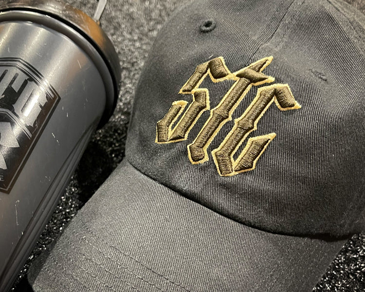Black cap with gold and brown logo and black blender bottle on a textured surface