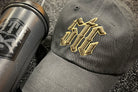 Black cap with gold and brown logo and black blender bottle on a textured surface