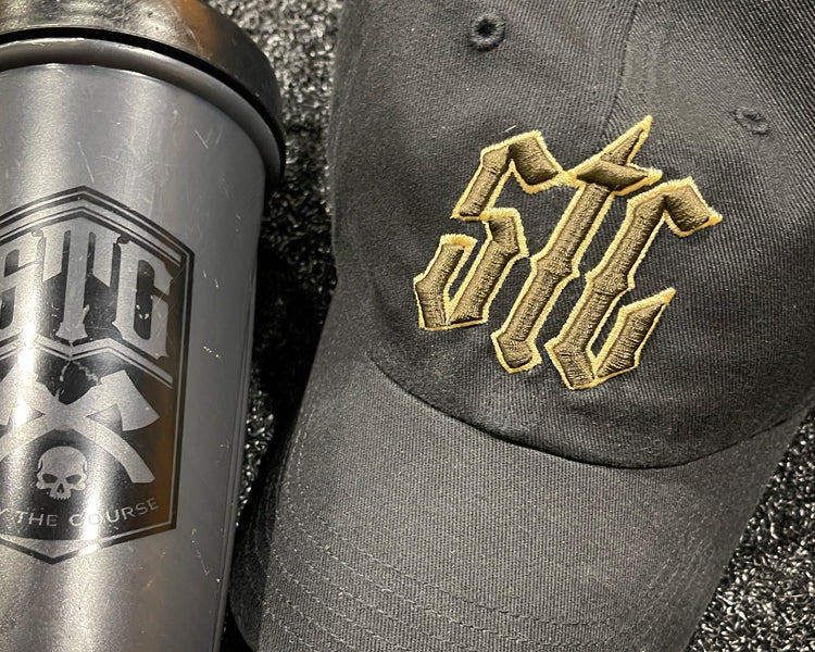 Black tumbler and black cap with gold and brown logo on a textured surface