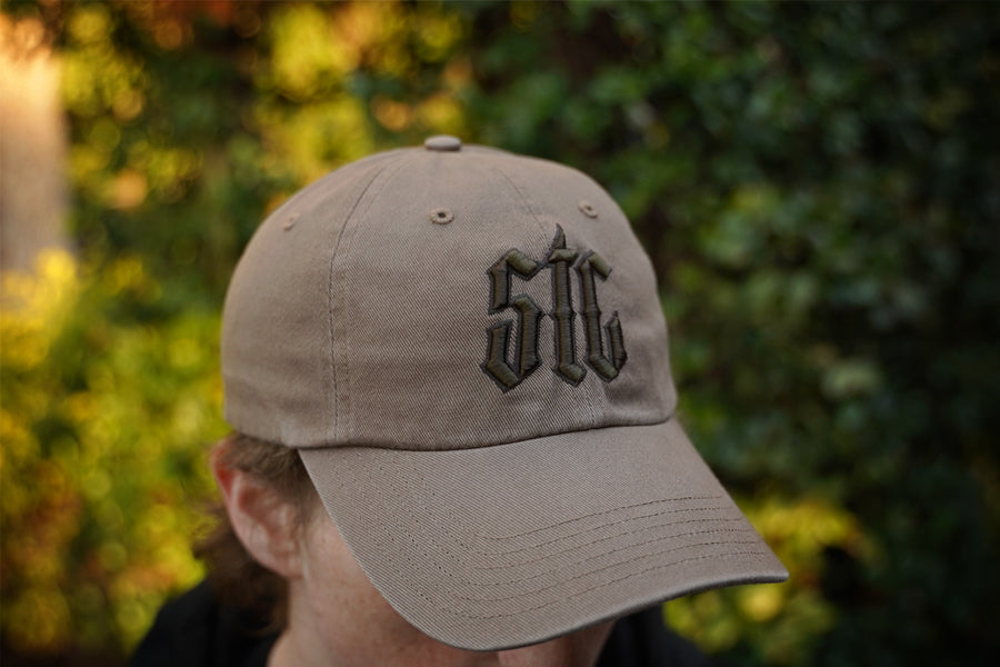 Beige cap with 'STC' logo worn by a person against a blurred green background