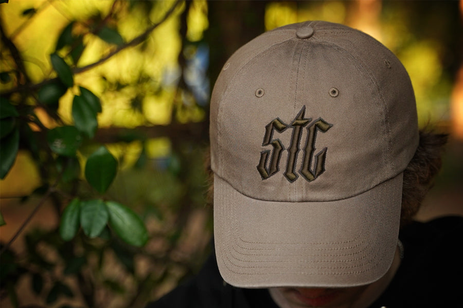 Beige cap with 'STG' logo held by a person against a blurred natural background