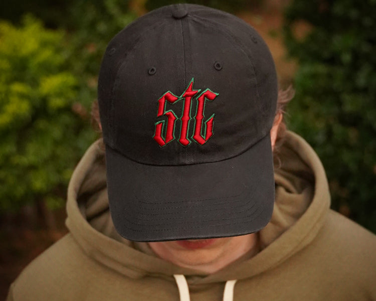 Person wearing a black cap with red and green logo, blurred green background