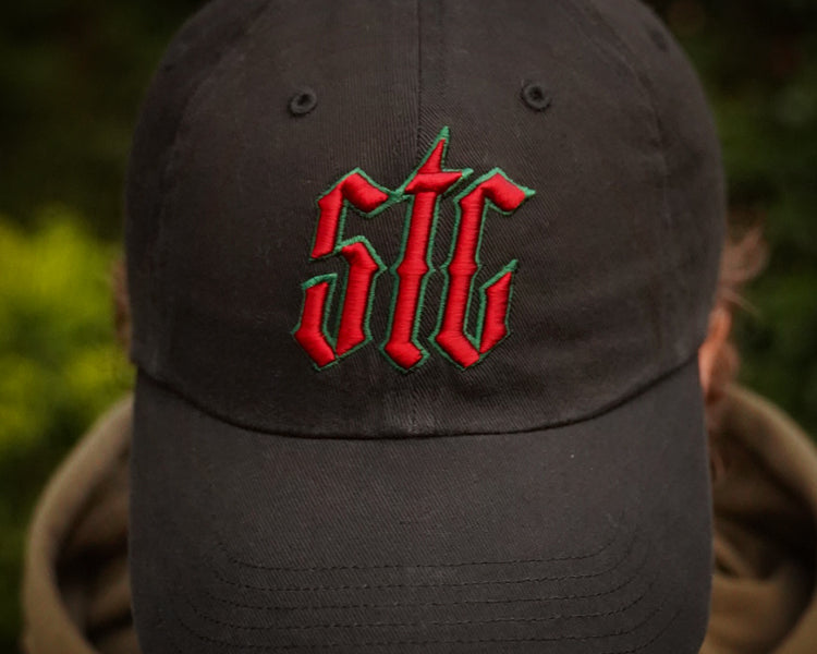 Black cap with red and green logo worn by a person against a blurred natural background