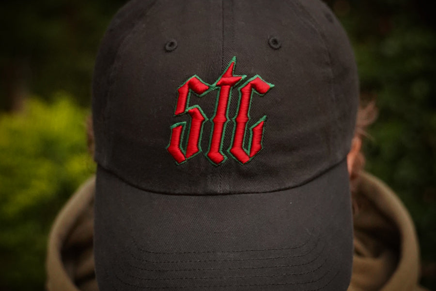 Black cap with red and green logo worn by a person against a blurred natural background