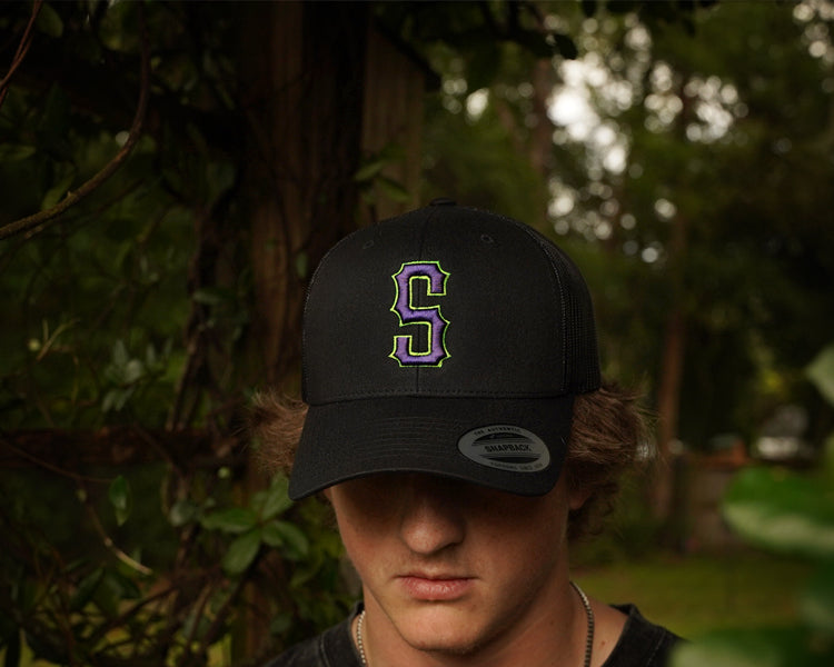 Person wearing a black cap with a 'S' logo in a forest setting