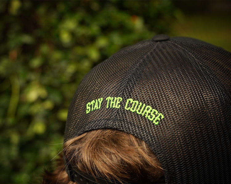 Person wearing a cap with 'Stay the Course' text against a blurred green background
