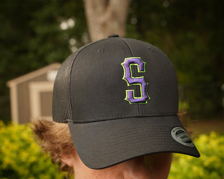 Person wearing a black cap with a purple and green logo outdoors