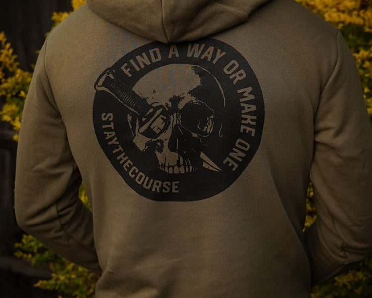 Person wearing a hoodie with a skull design and text on the back, standing in front of blurred greenery.