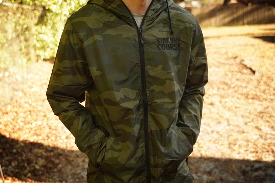 Person wearing a camouflage jacket with 'Stay the Course' text in an outdoor setting