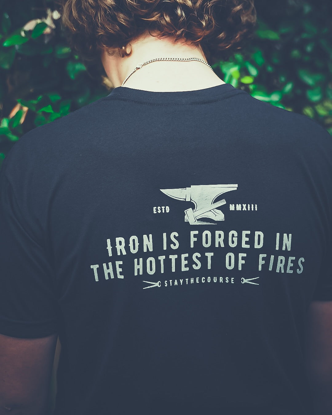 Person wearing a black t-shirt with a motivational quote and an anvil graphic.