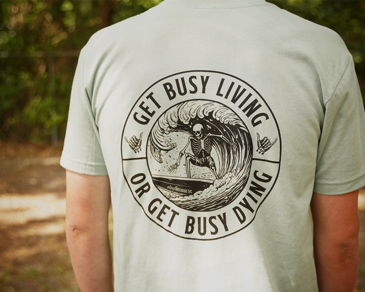 Person wearing a green shirt with black graphic that says "get busy living or get busy dying"