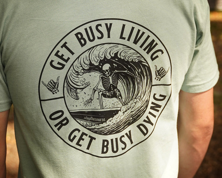 Person wearing a green shirt with black graphic that says "get busy living or get busy dying"