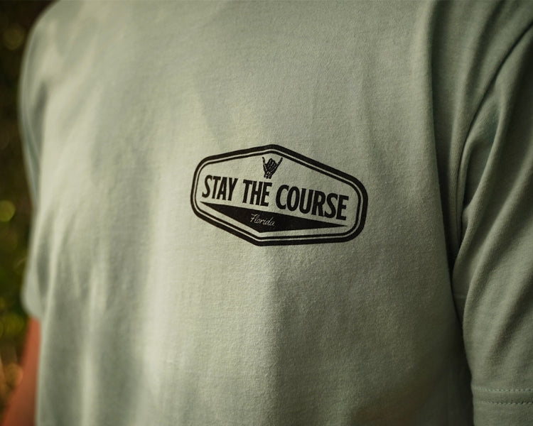 Person wearing a green shirt with black graphic that says "Stay the Course"