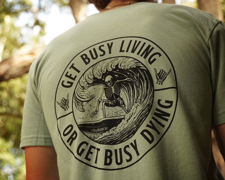 Person wearing a green shirt with black graphic that says "get busy living or get busy dying"