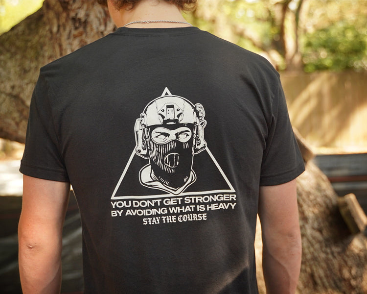 Person wearing a black t-shirt with a graphic design and text on the back, standing outdoors.