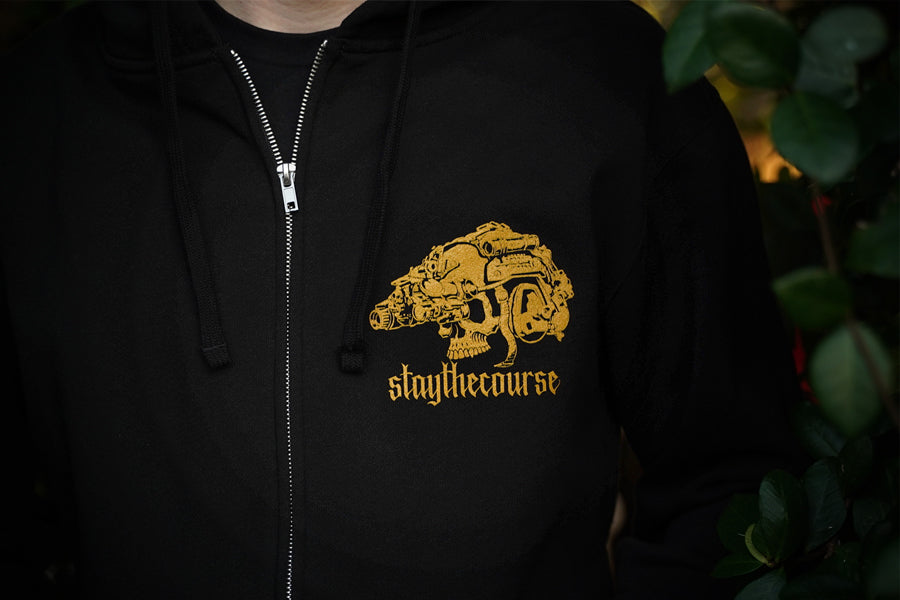 Black hoodie with gold graphic and text 'staythecourse' on a dark background