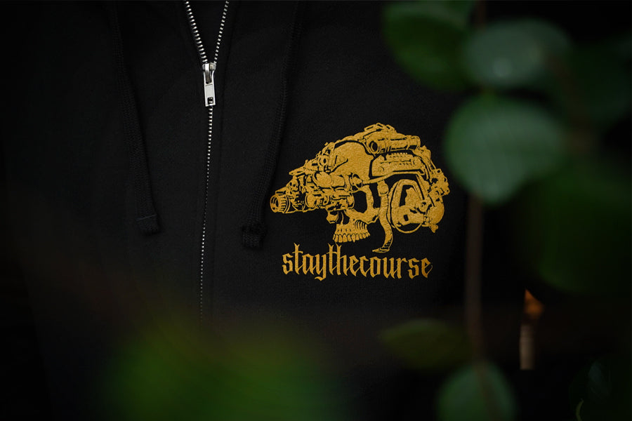 Black hoodie with gold graphic and 'staythecourse' text on a dark background
