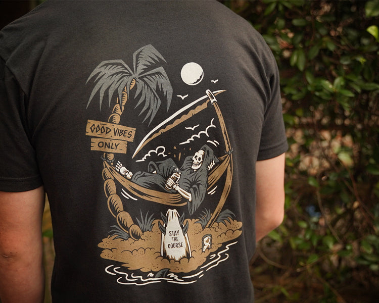 Person wearing a black t-shirt with a graphic design on the back, featuring a reaper and palm trees.
