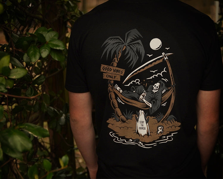 Person wearing a black t-shirt with a graphic design of a reaper chilling in a hammock, and palm trees on a dark background.