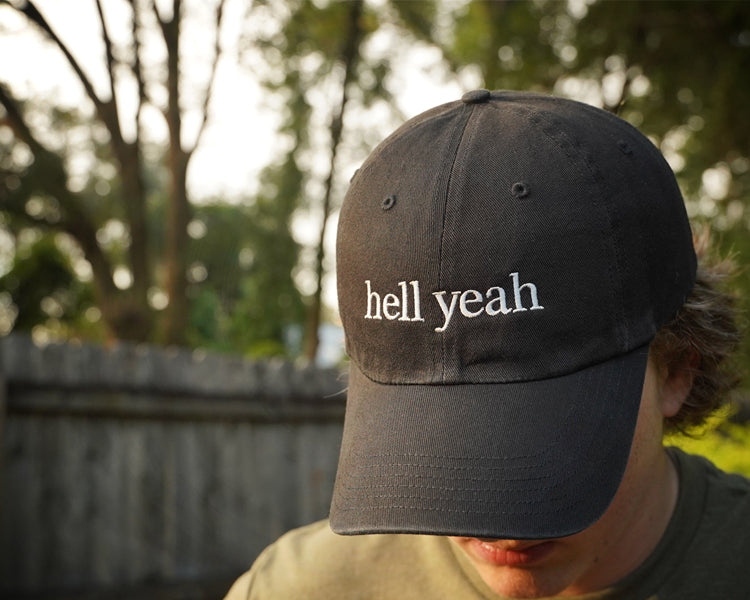 Person wearing a black cap with 'hell yeah' text outdoors