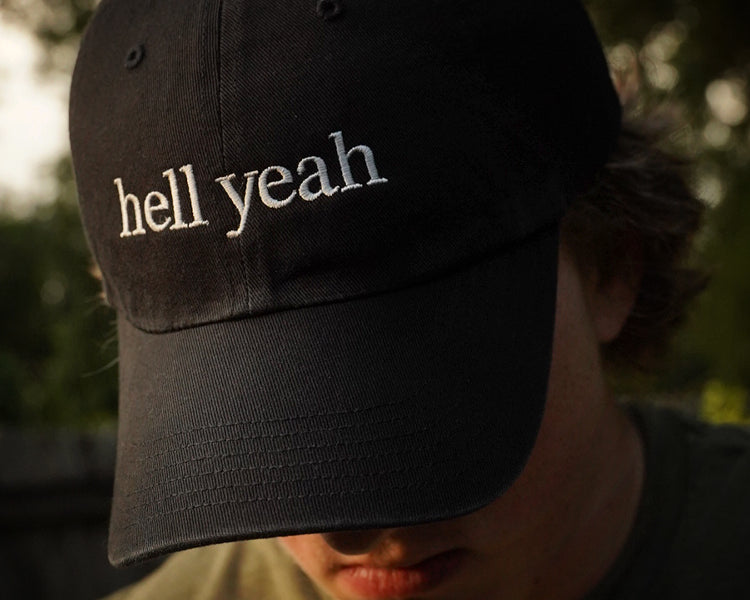 Black cap with 'hell yeah' text worn by a person outdoors