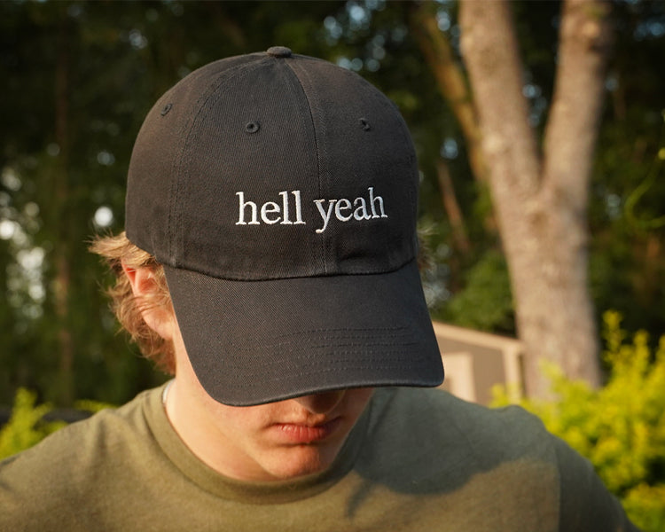 Person wearing a black cap with 'hell yeah' text outdoors