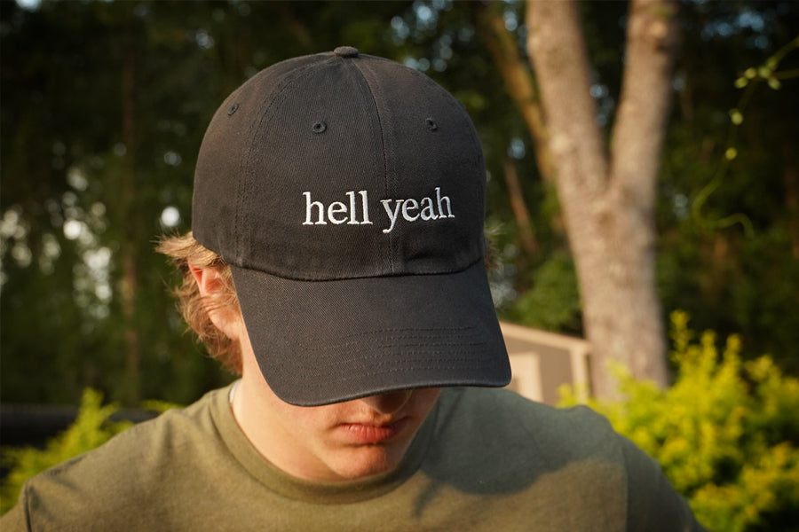 Person wearing a black cap with 'hell yeah' text outdoors