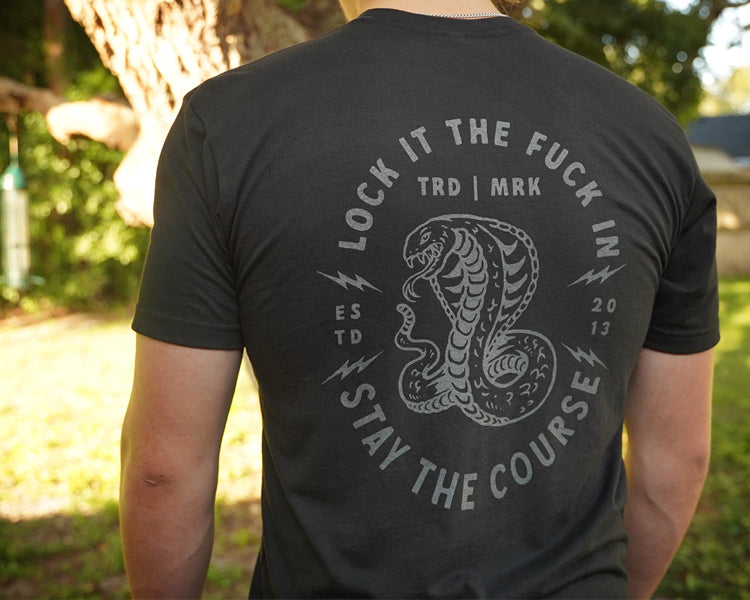 Person wearing a black t-shirt with a snake graphic and text outdoors