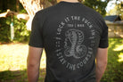 Person wearing a black t-shirt with a snake graphic and text outdoors