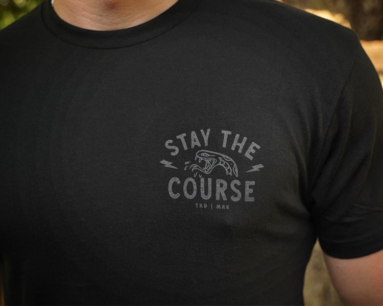 Black t-shirt with 'Stay the Course' text and graphic on a blurred background