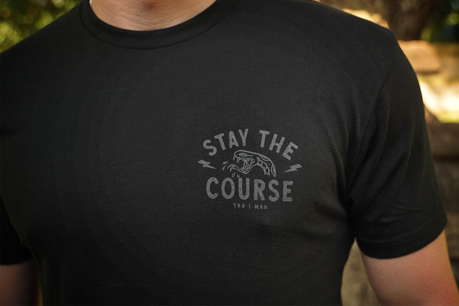 Black t-shirt with 'Stay the Course' text and graphic on a blurred background