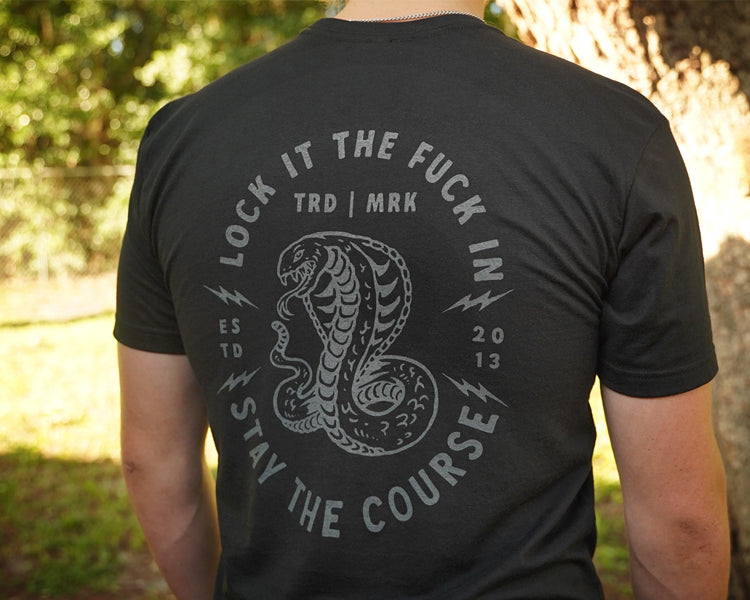 Person wearing a black t-shirt with a snake graphic and text outdoors