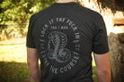 Person wearing a black t-shirt with a snake graphic and text outdoors